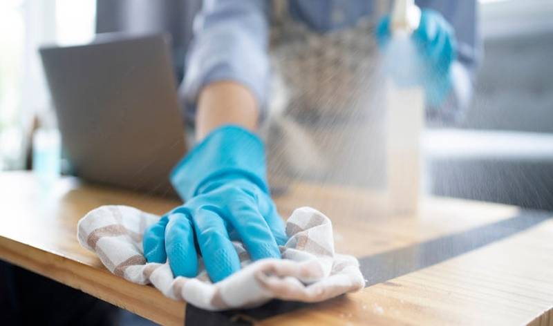 Woman in blue gloves spraying on table