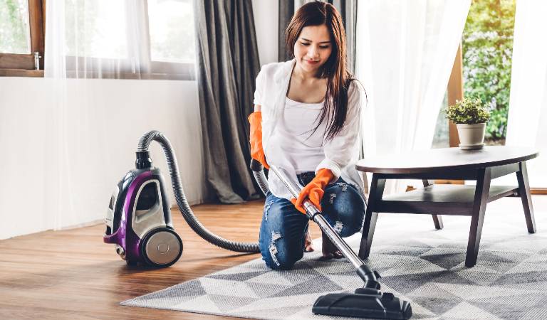 Woman in white top and blue dress vacuuming floor inside a room