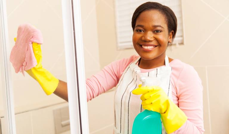 Woman in pink dress holding green bottle scrubbing glass door