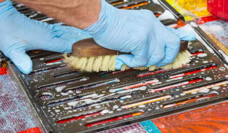 A man in blue gloves scrubbing grill grates with a brush.