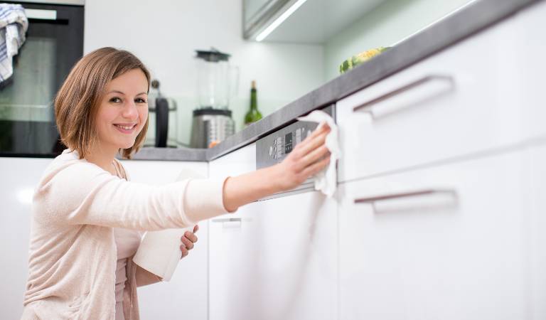 Woman in white dress scrubbing kitchen cabinets using a cloth