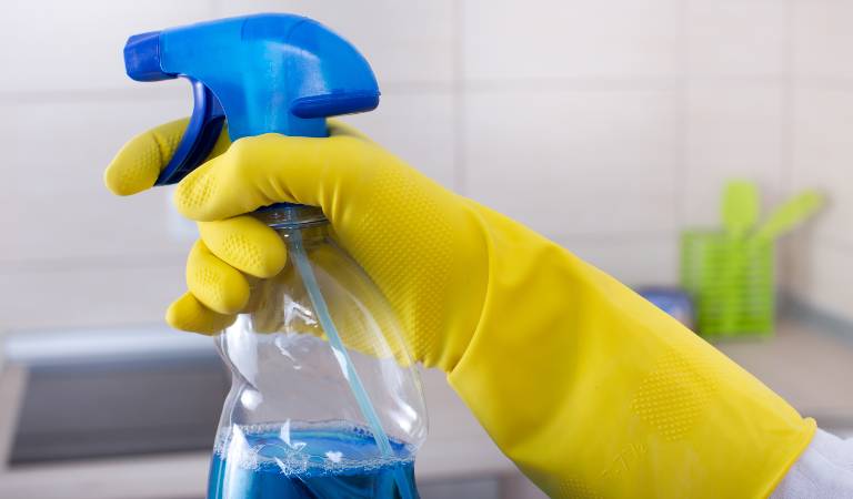 Hand in yellow gloves holding a bottle filled with natural solution.