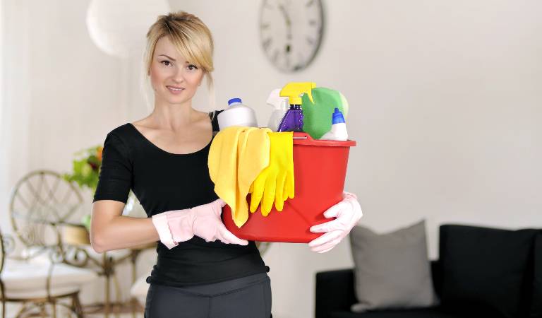 Lady in black dress holding a red basket filled with tools, gloves, products.