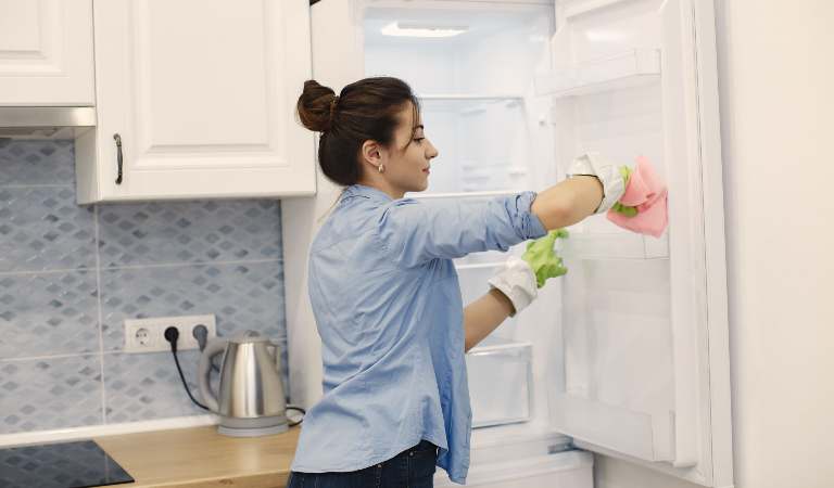 Woman in plane shirt cleaning refrigerator inside her kitchen.