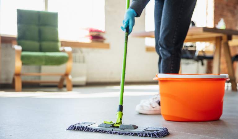 Man cleaning floor using a mop with orange basket on the floor.