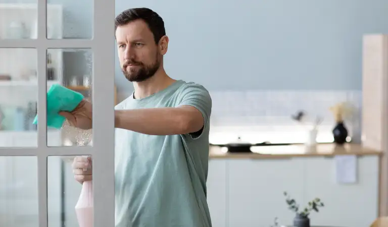 Man holding a white bottle in his hand and cleaning door.