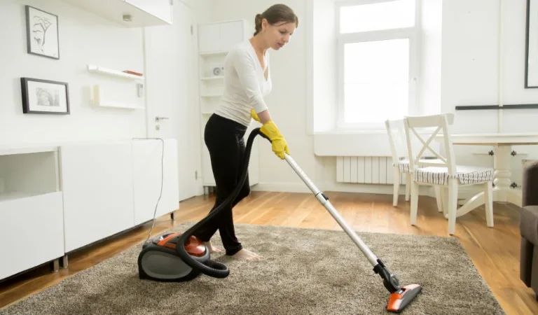 Woman in casual wear vacuum cleaning the carpet