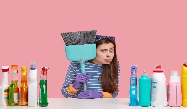young cleaning service employee holds broom, uses numerous cleaning substances, arent ready to start working, has negative attitude to work