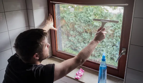 Man washes a window in a house using scraper