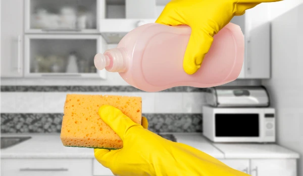 Woman's hand in protective glove with bottle of dishwashing liquid