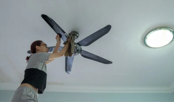 A woman cleaning a ceiling fan with cloth